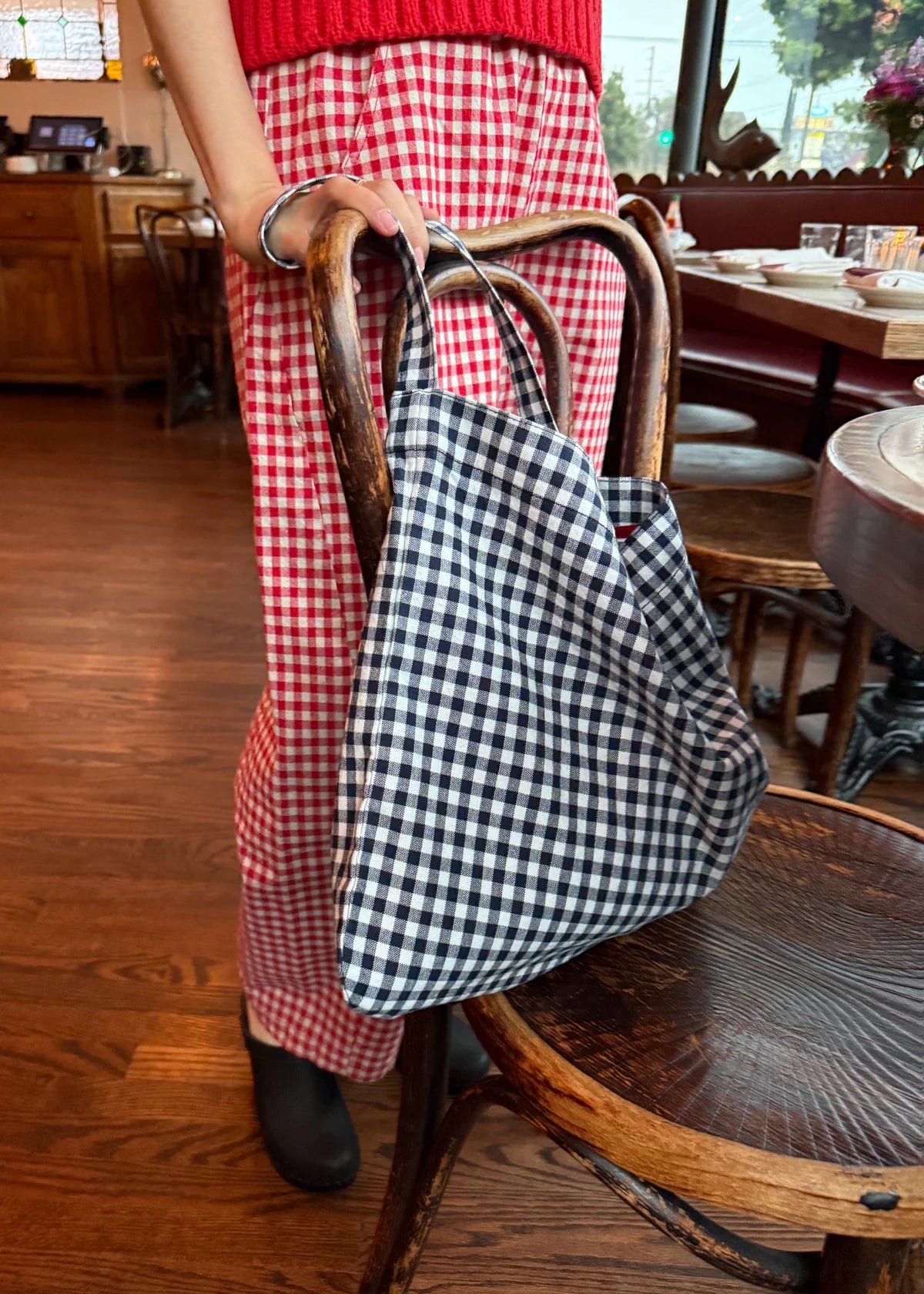 Person wearing a red checkered outfit with a black and white checkered bag in a restaurant setting