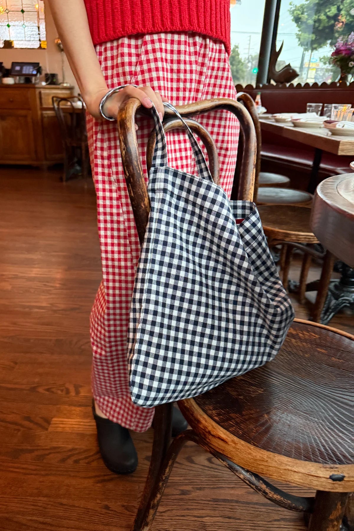 Person wearing a red checkered outfit with a black and white checkered bag in a restaurant setting