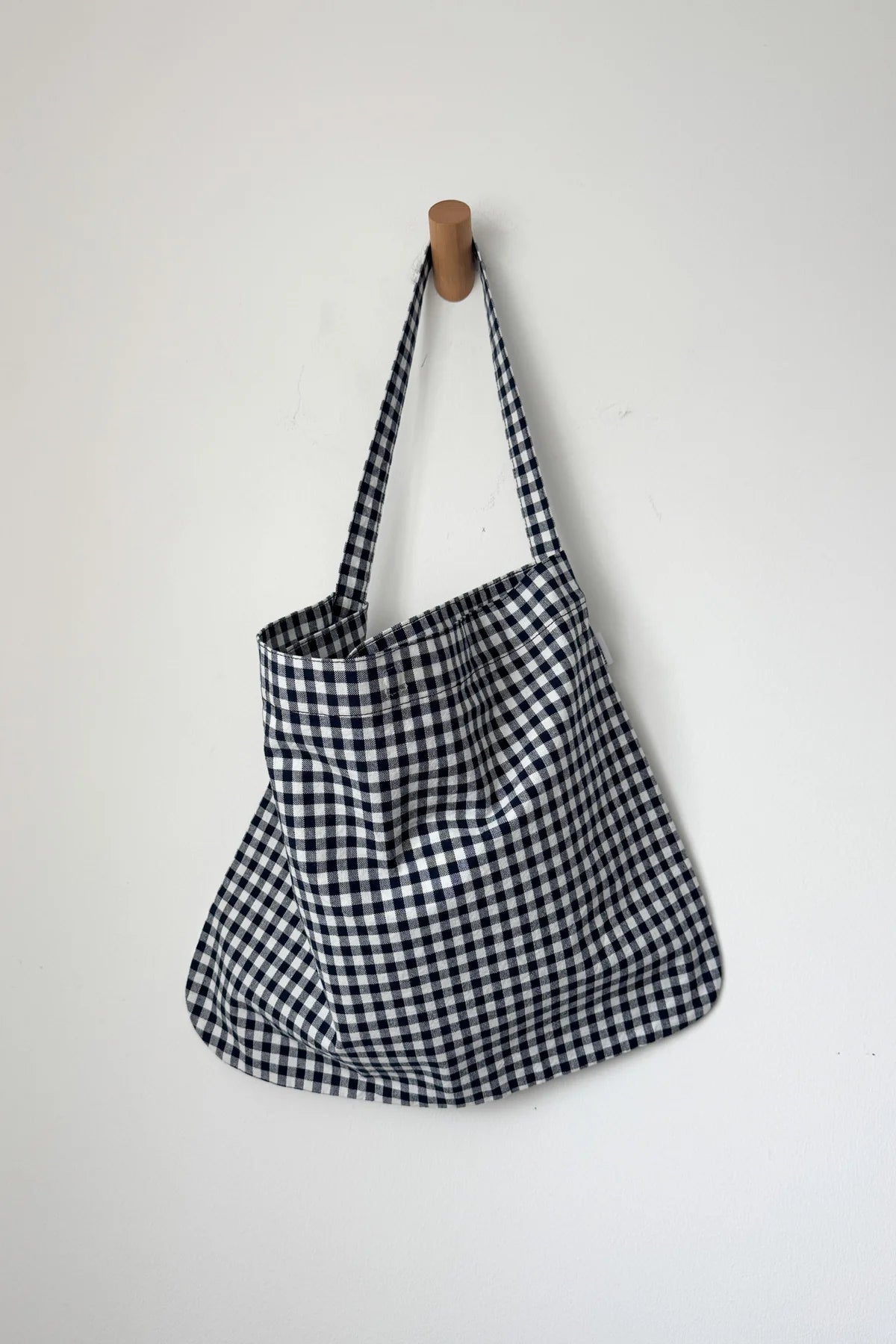 Black and white checkered bag hanging on a wooden hook against a white background