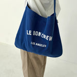 Blue bag with 'LE BON CREW' text held by a person wearing beige pants on a white background
