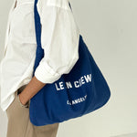 Person holding a blue bag with 'LE BON CREW' branding against a white background