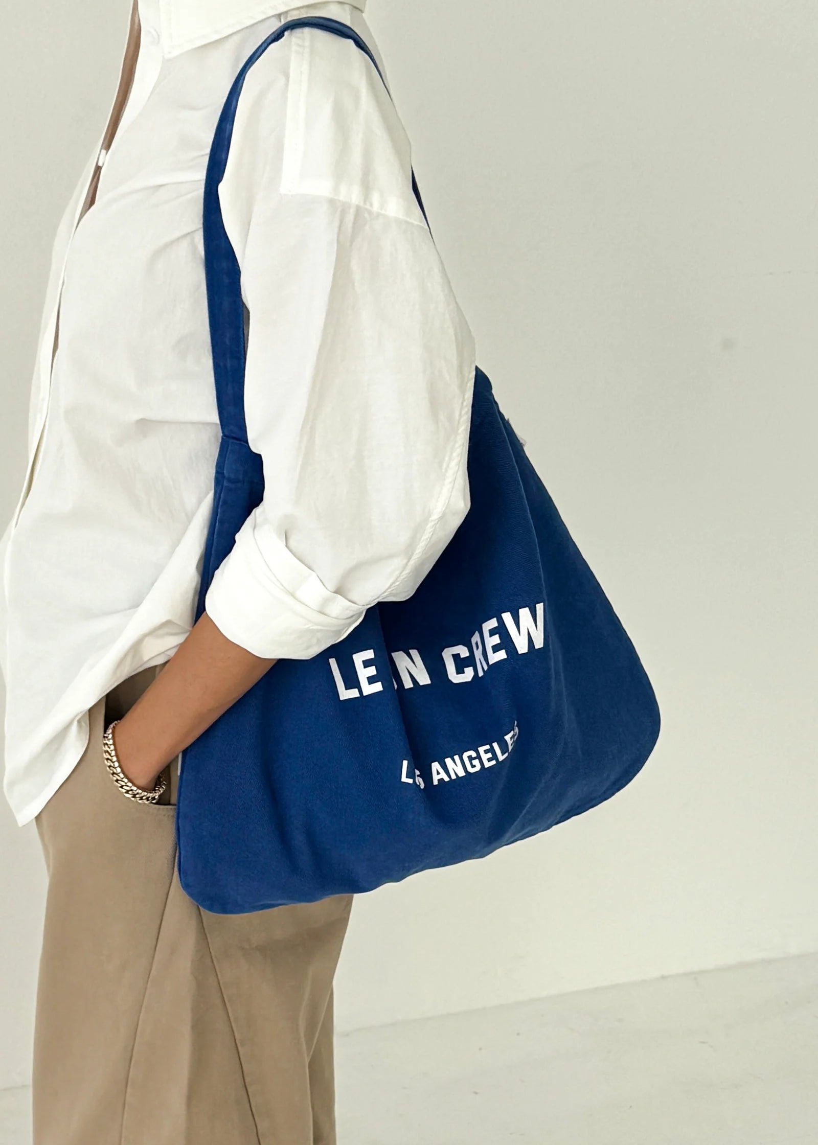 Person holding a blue bag with 'LE BON CREW' branding against a white background