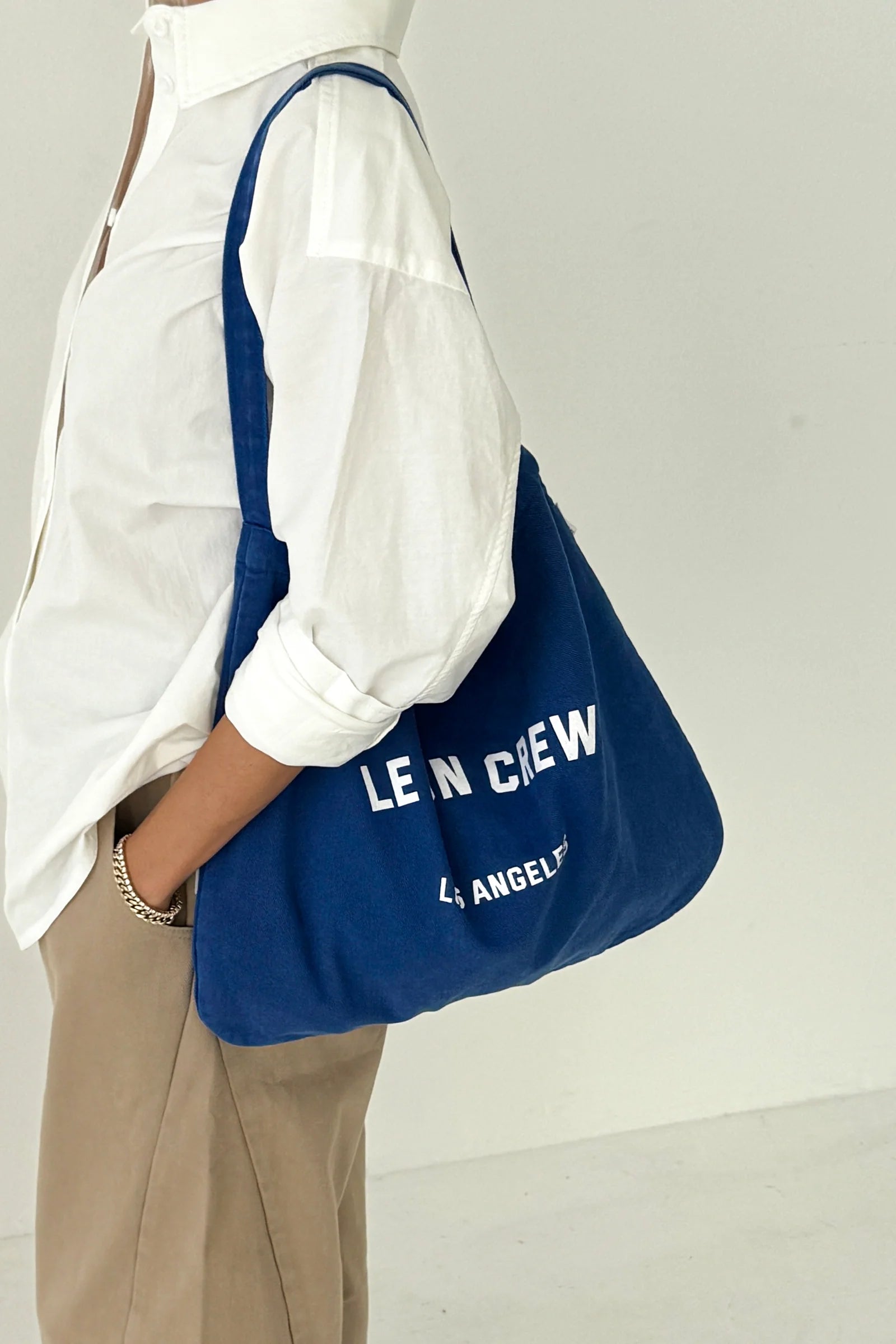 Person holding a blue bag with 'LE BON CREW' branding against a white background
