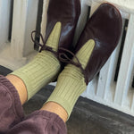 Brown leather shoes and green socks being worn, with a white railing in the background.