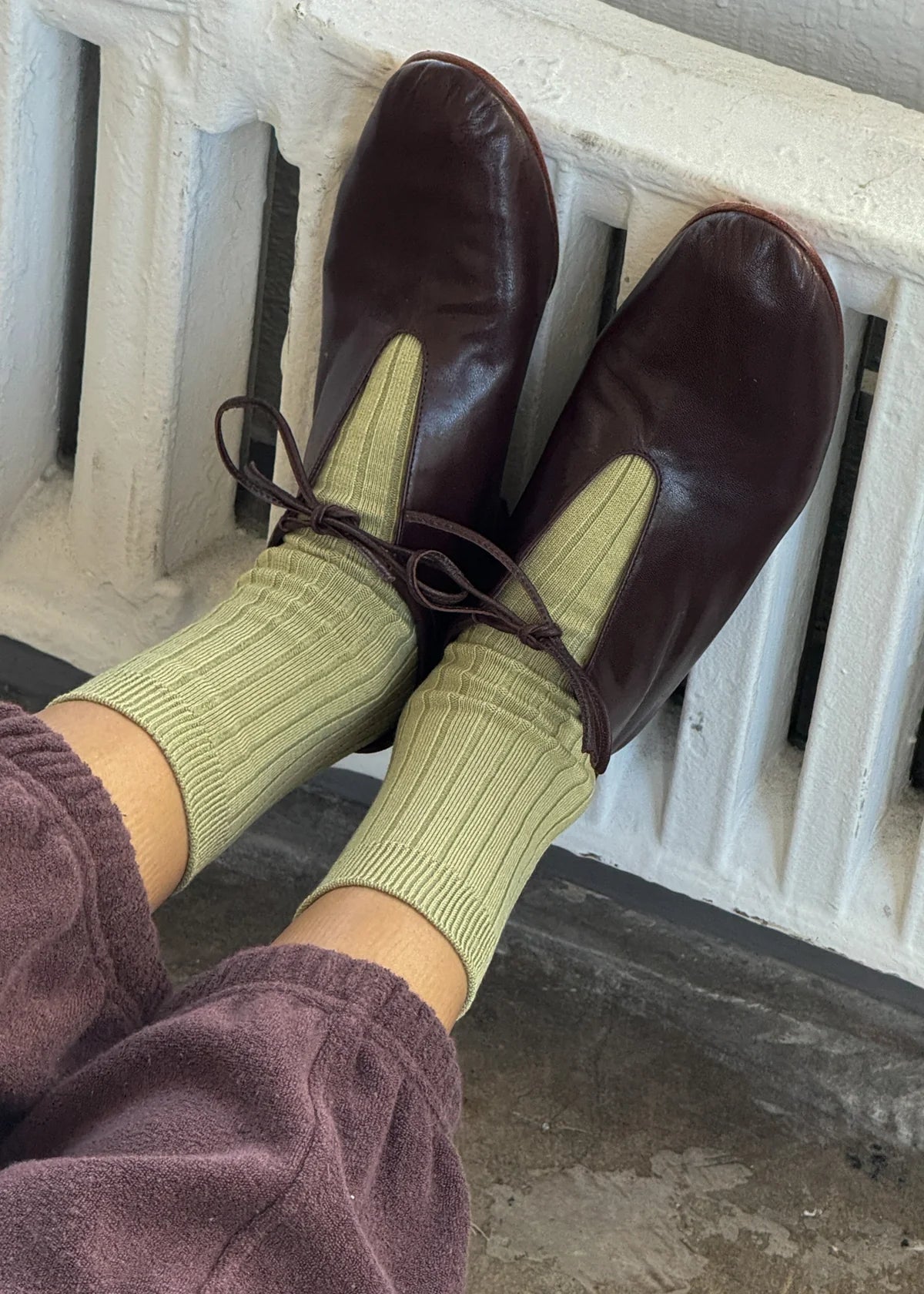 Brown leather shoes and green socks being worn, with a white railing in the background.