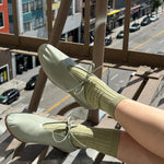 Person wearing light green shoes and socks on a balcony with a city street view.