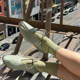 Person wearing light green shoes and socks on a balcony with a city street view.