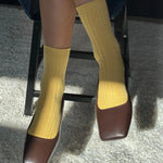 Yellow socks and brown shoes on a person sitting on a chair.