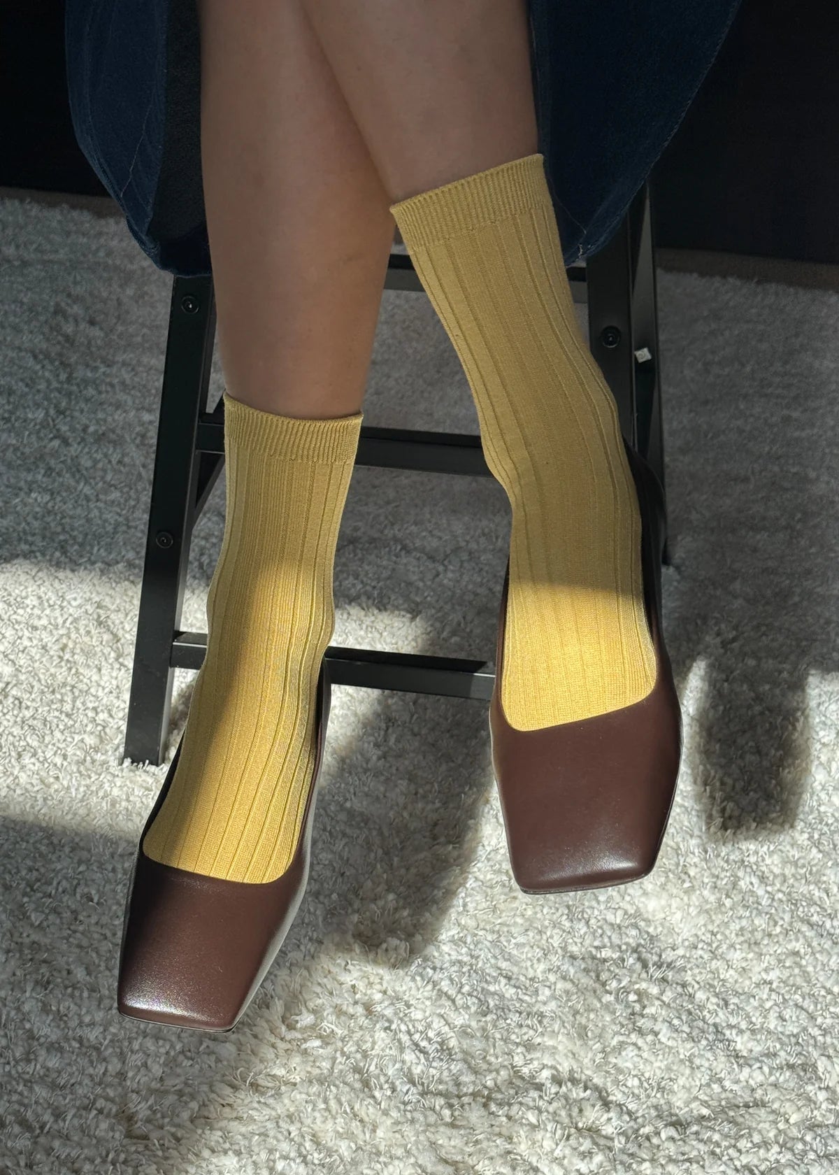 Yellow socks and brown shoes on a person sitting on a chair.
