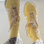 Yellow sneakers with white stripes worn with patterned pants on a light background