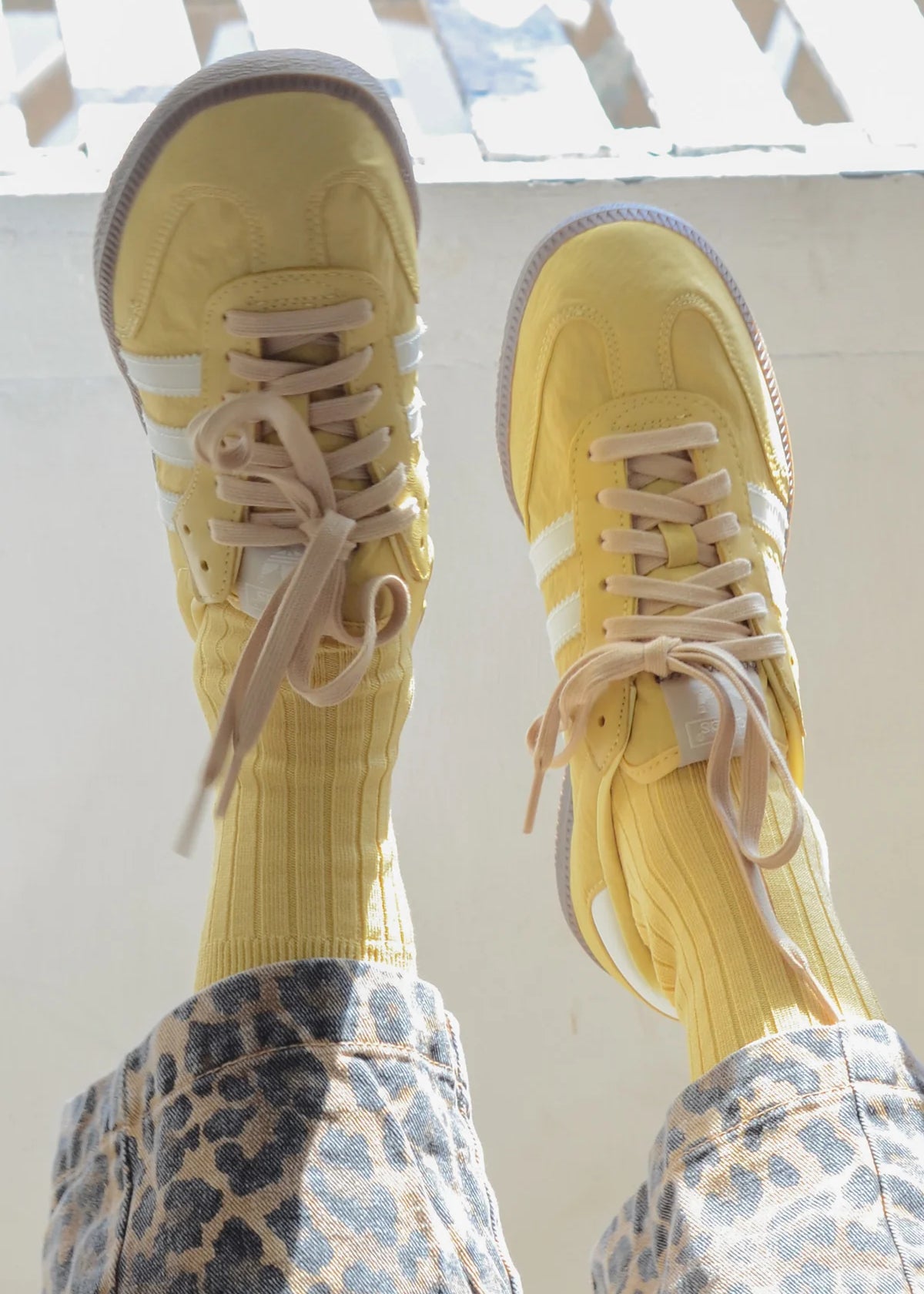 Yellow sneakers with white stripes worn with patterned pants on a light background