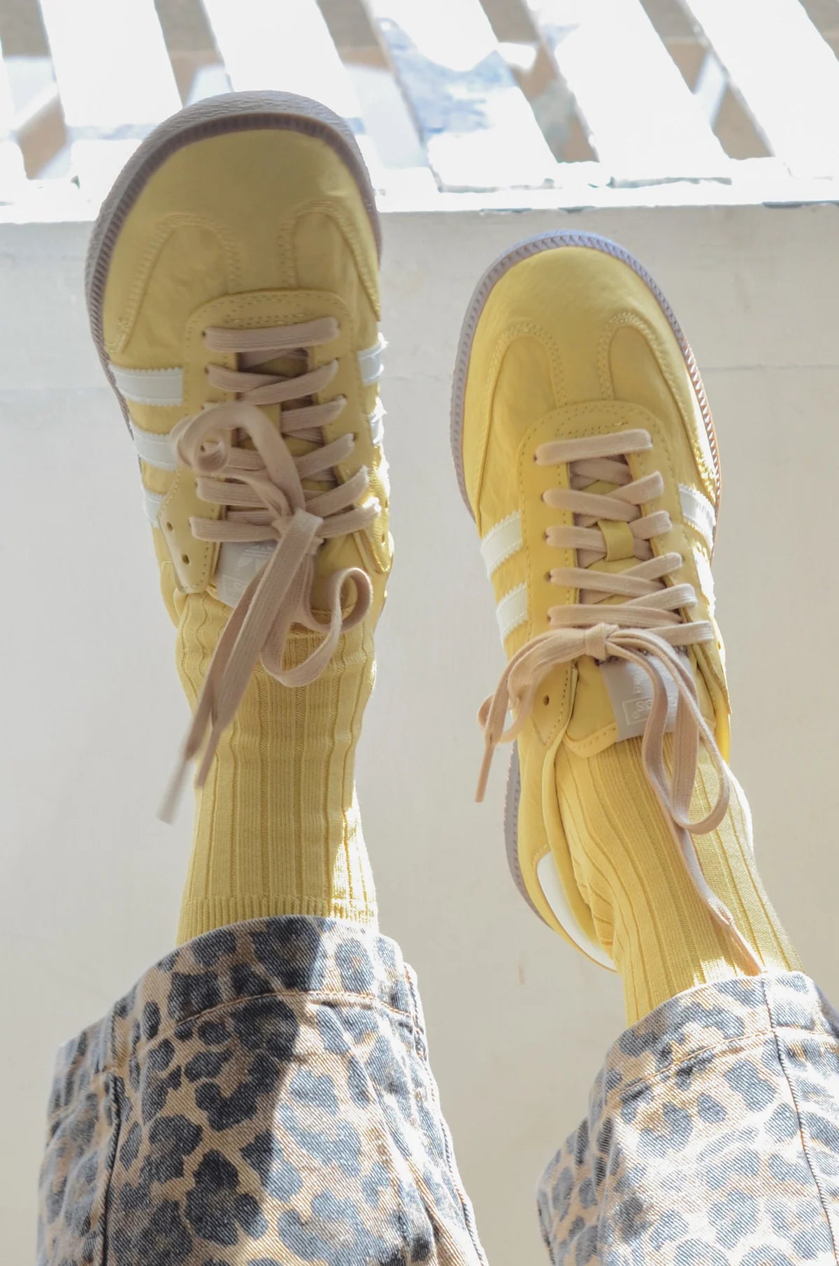 Yellow sneakers with white stripes worn with patterned pants on a light background