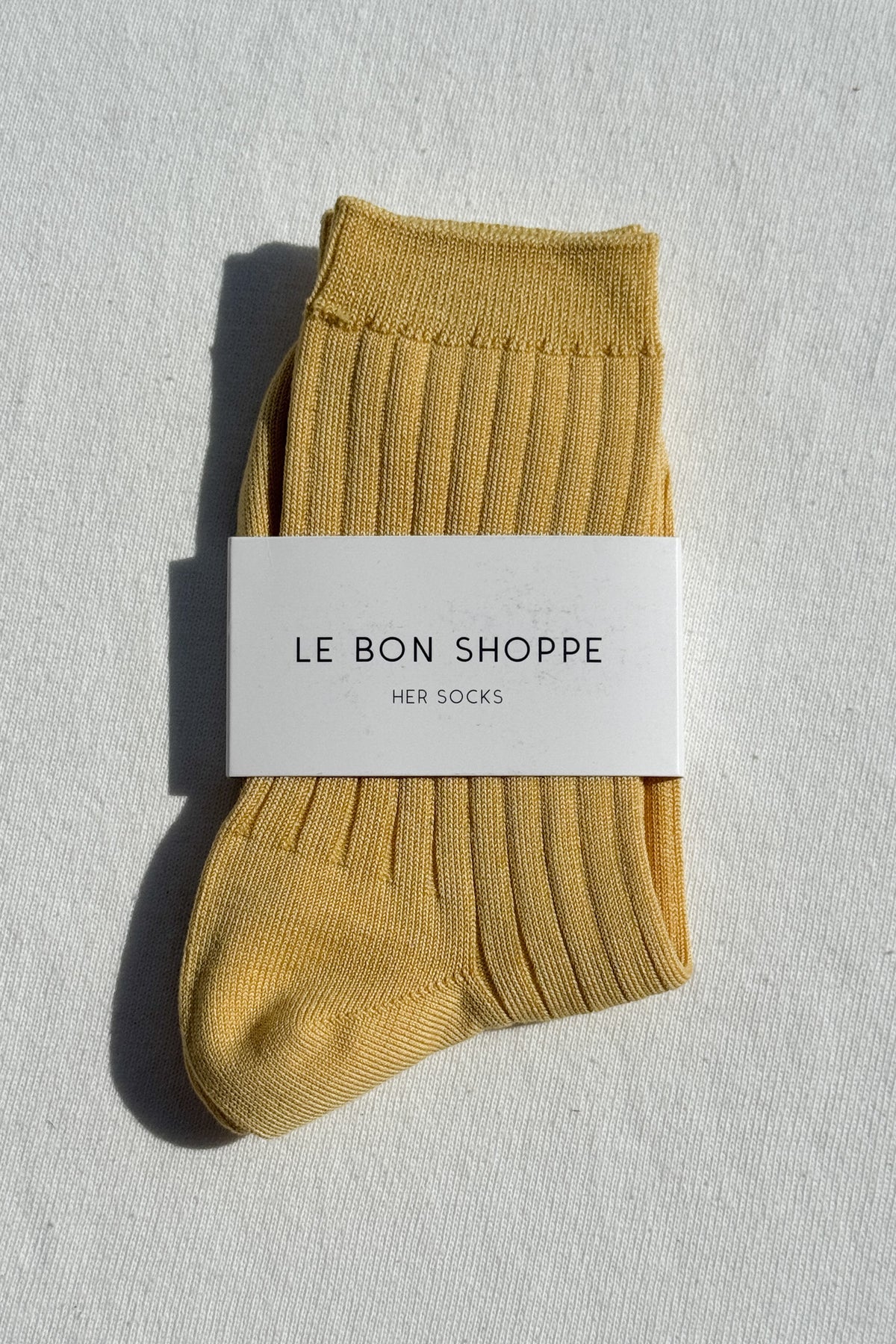 Mustard yellow sock with 'Le Bon Shoppe' label on a light gray background