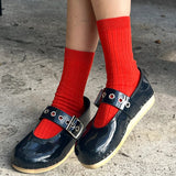 Person wearing navy shoes with buckles and red socks on a concrete surface