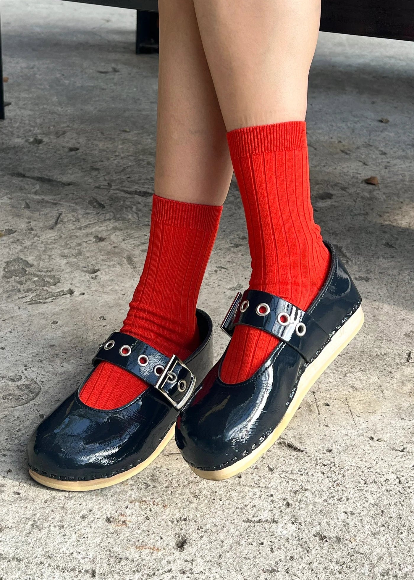 Person wearing navy shoes with buckles and red socks on a concrete surface