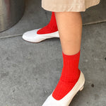 Person wearing red socks and white shoes on a concrete surface