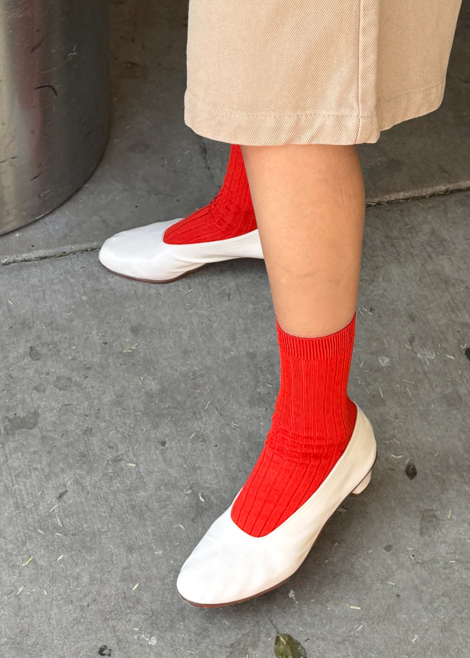 Person wearing red socks and white shoes on a concrete surface