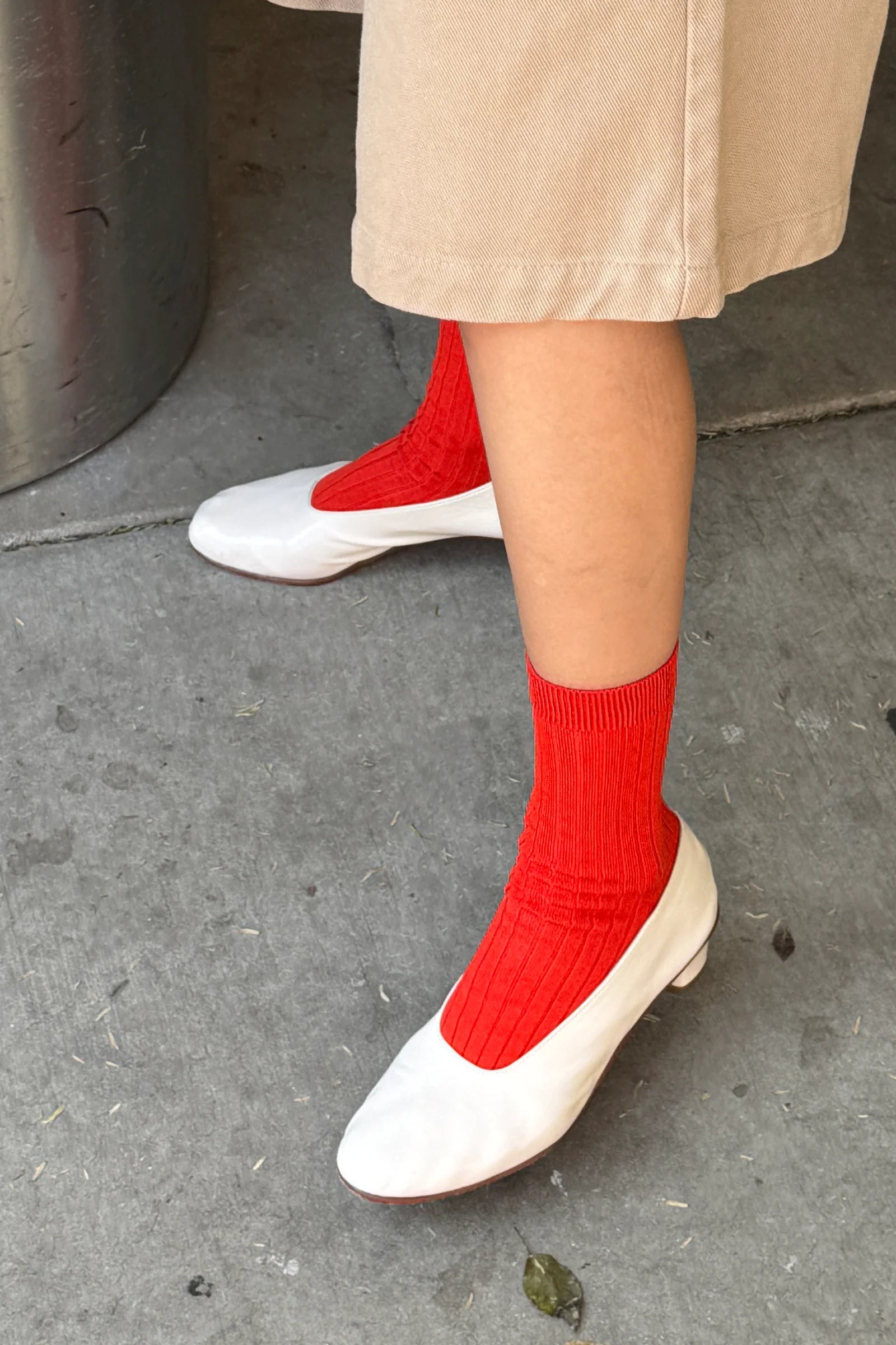 Person wearing red socks and white shoes on a concrete surface