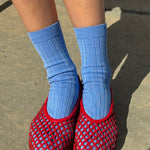 Person wearing blue socks and red mesh slippers on a concrete surface