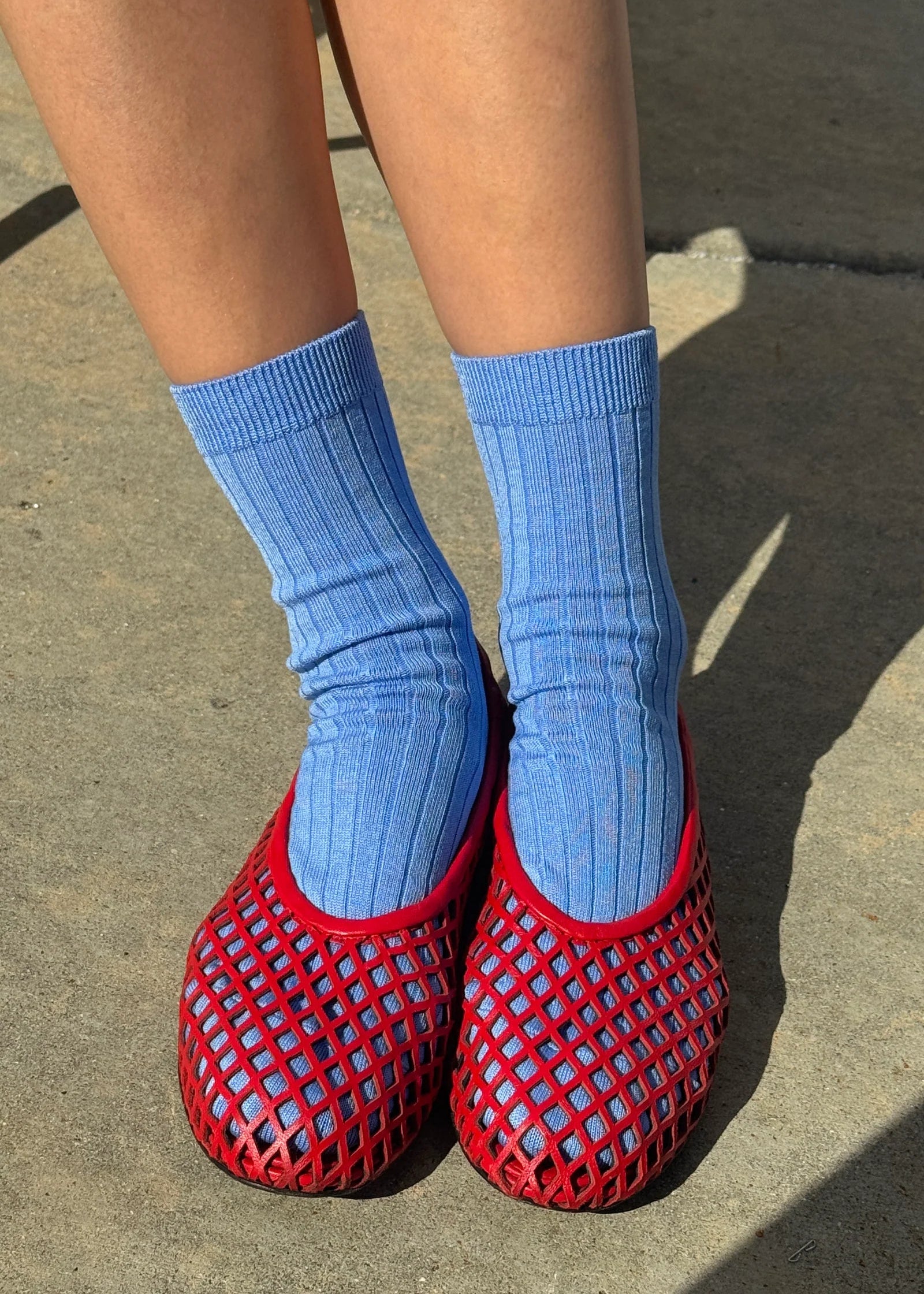 Person wearing blue socks and red mesh slippers on a concrete surface