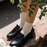 Person wearing black shoes and white socks standing on a stone surface with greenery around.