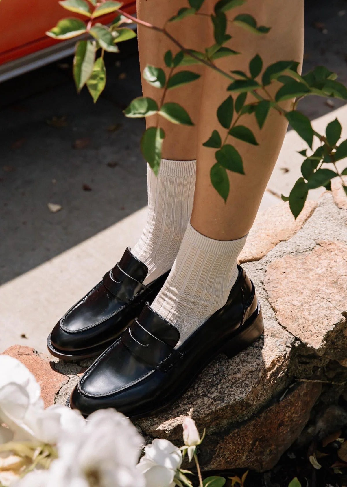 Person wearing black shoes and white socks standing on a stone surface with greenery around.