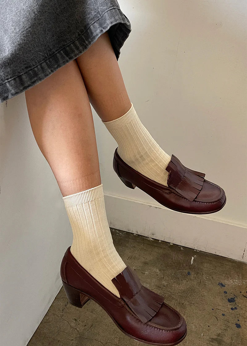 Person wearing brown loafers and beige socks against a neutral background