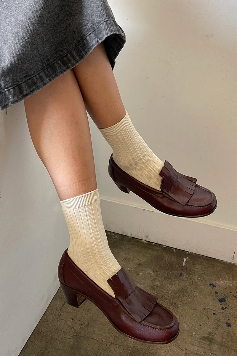Person wearing brown loafers and beige socks against a neutral background