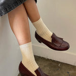 Person wearing brown loafers and beige socks against a neutral background