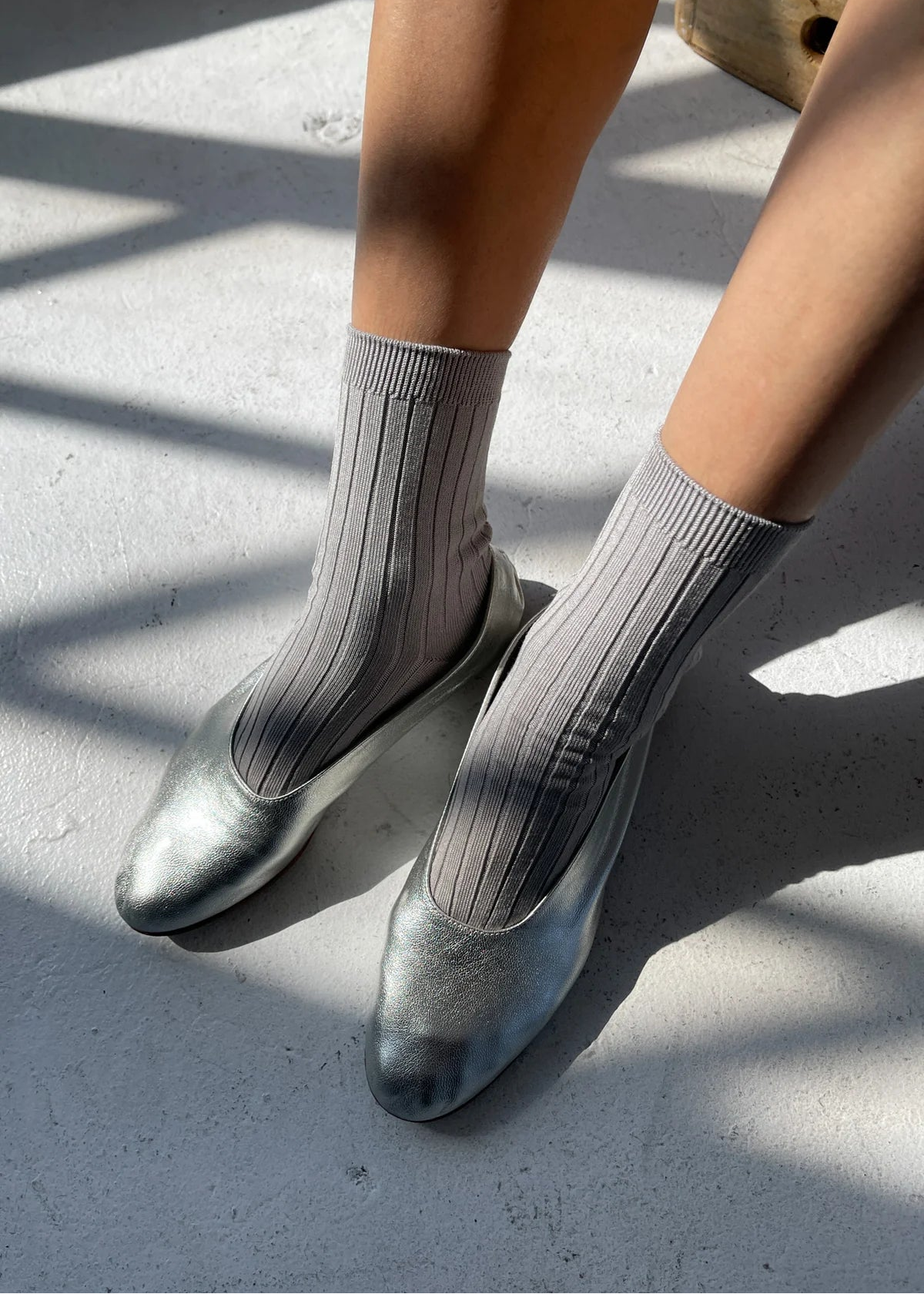 Person wearing silver shoes and gray socks on a concrete surface