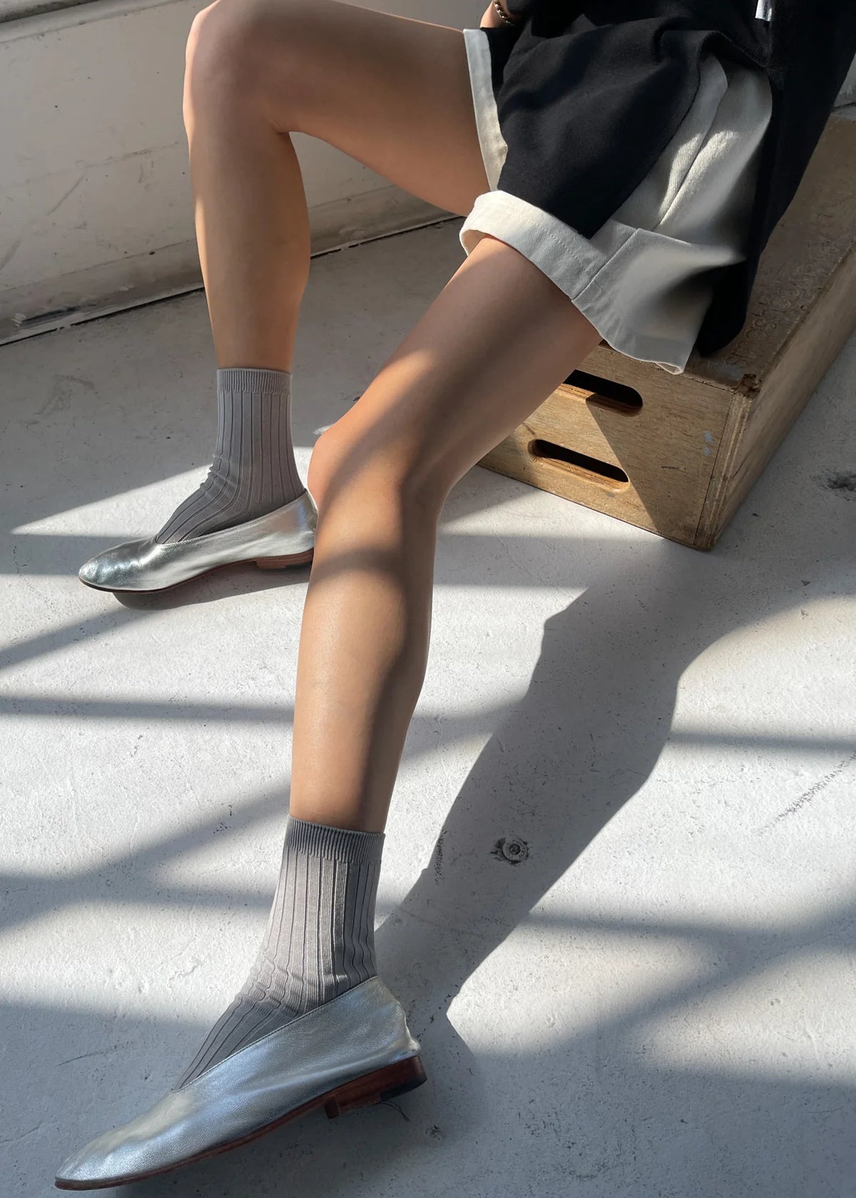 Person wearing gray socks and silver shoes sitting on a concrete surface.