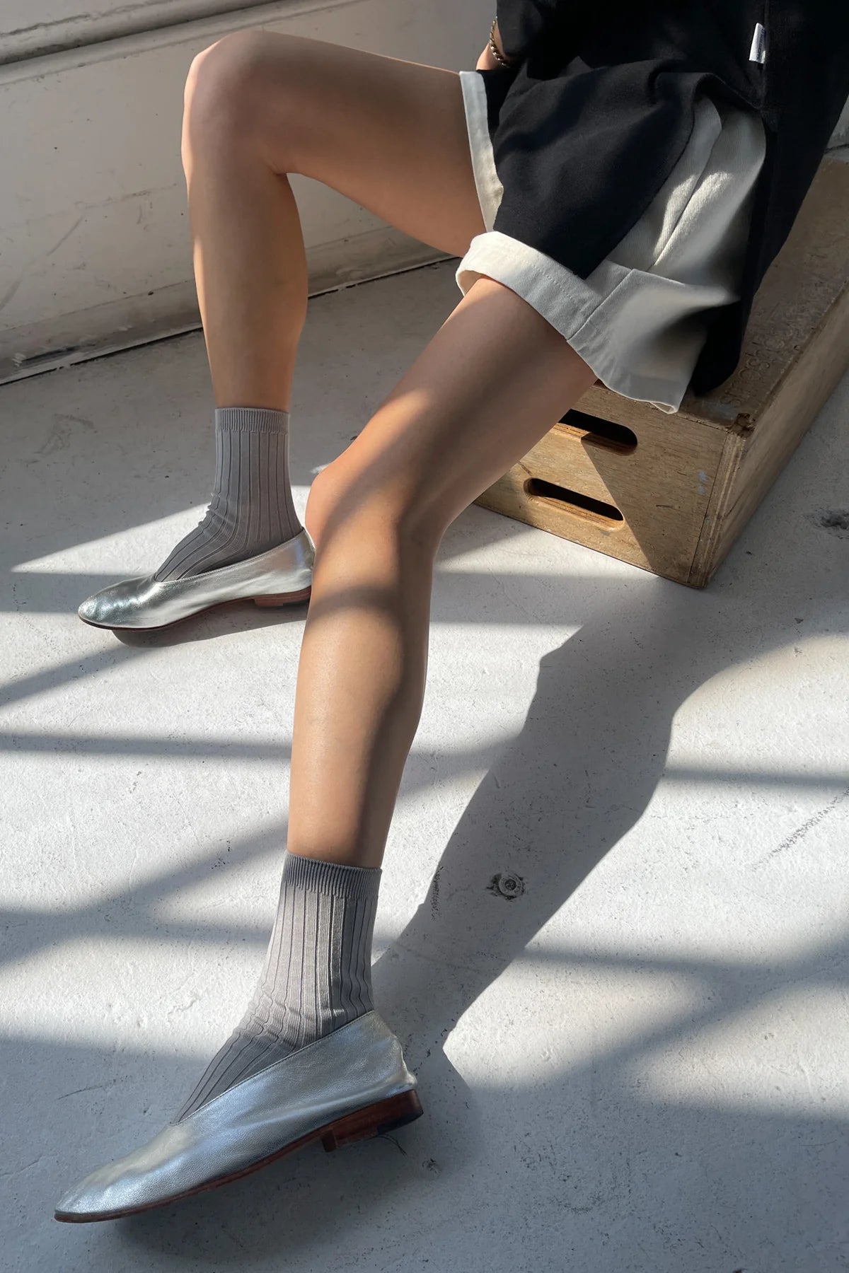Person wearing gray socks and silver shoes sitting on a concrete surface.