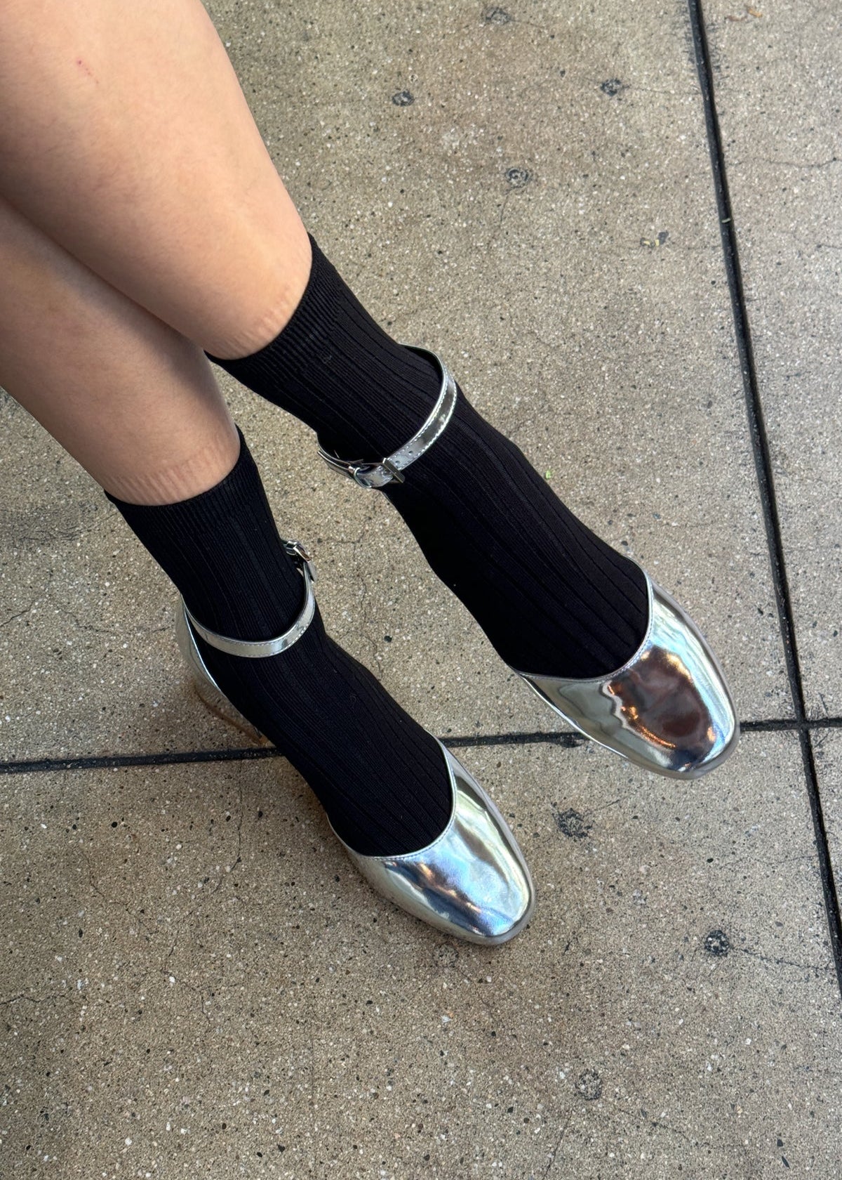 Person wearing black socks and silver shoes on a concrete surface