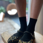 Person wearing leopard print slippers and black socks on a wooden chair.