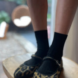 Person wearing leopard print slippers and black socks on a wooden chair.
