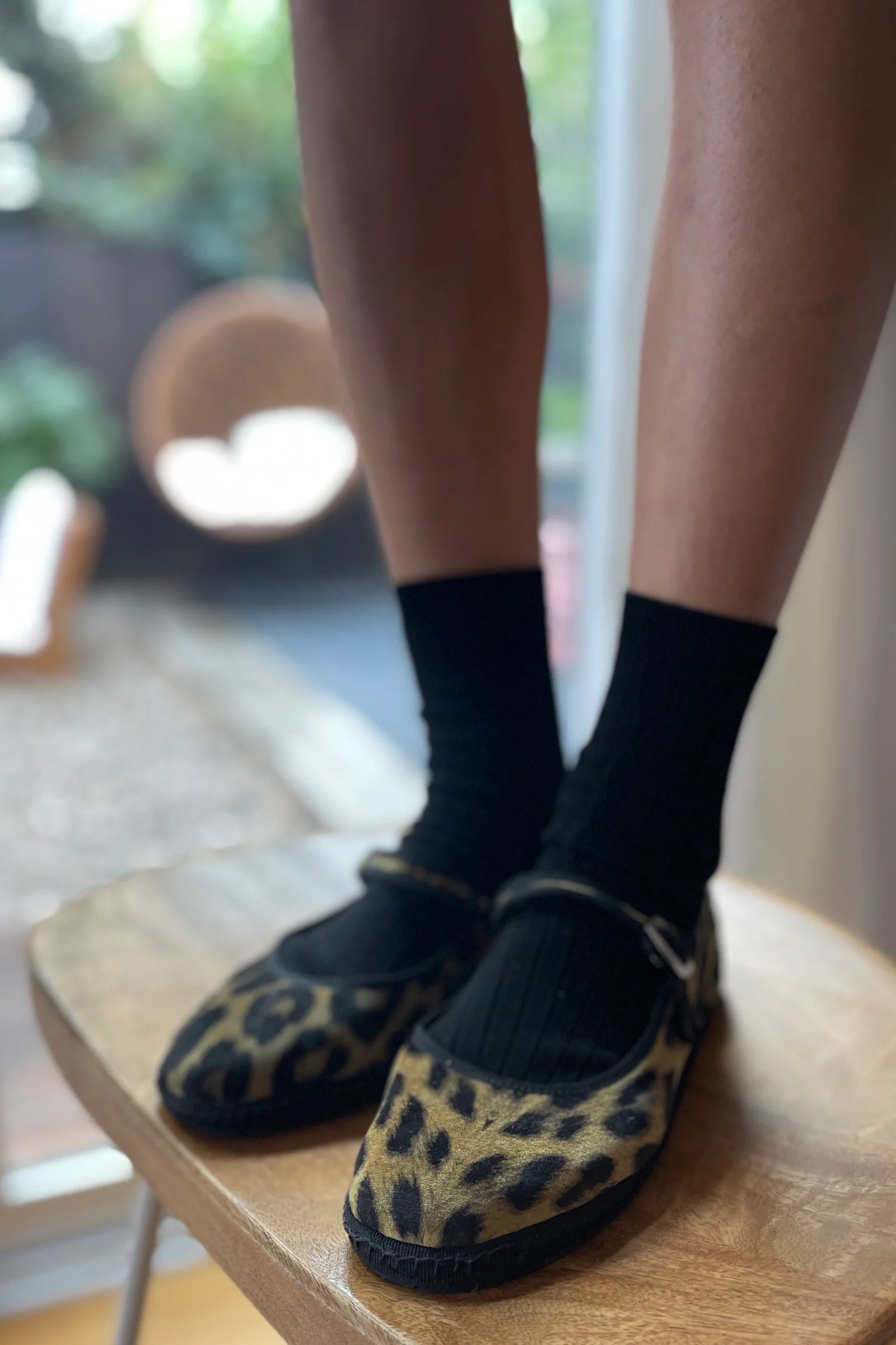 Person wearing leopard print slippers and black socks on a wooden chair.