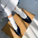 Person wearing black shoes and white socks on a wooden stool.