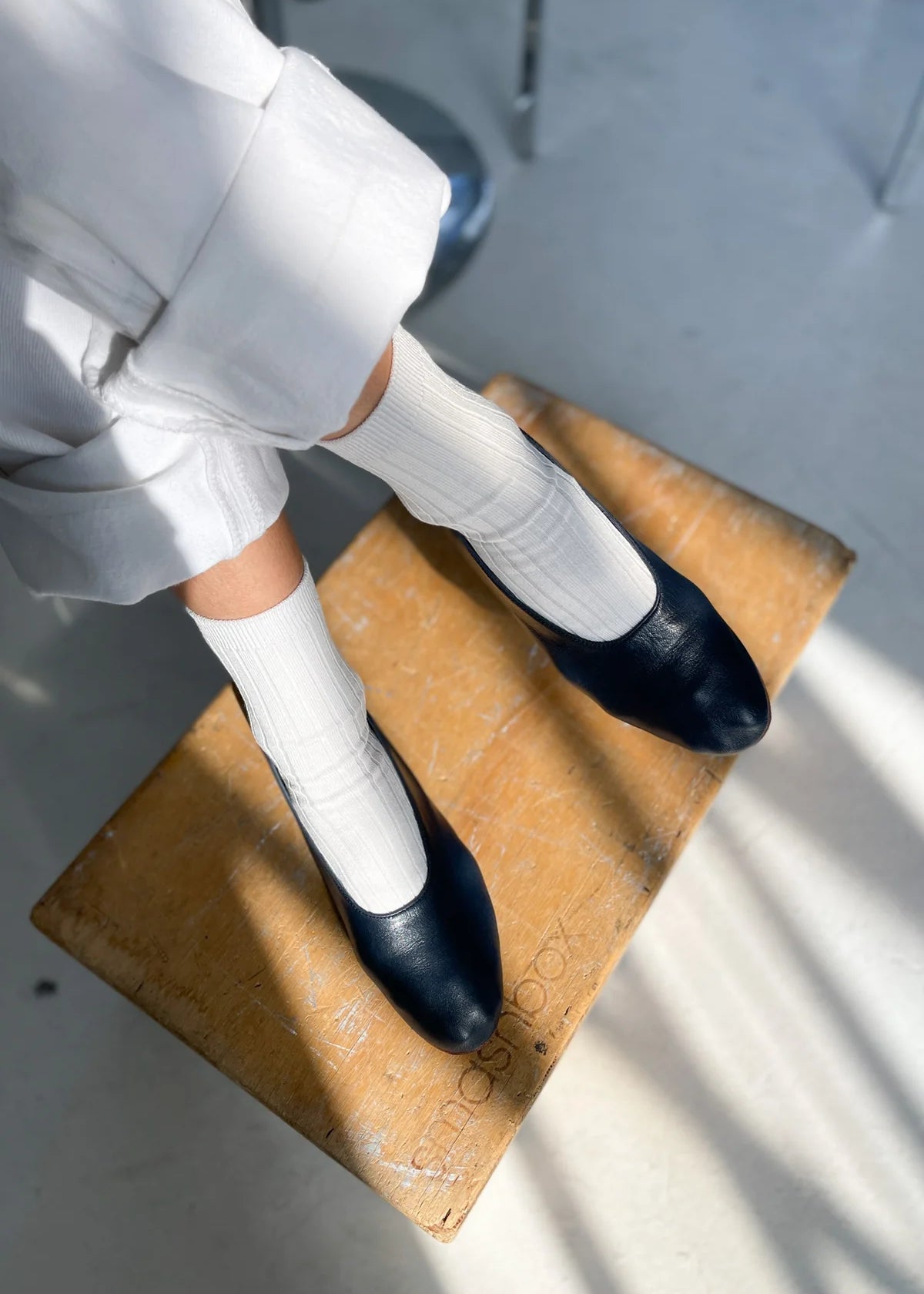 Person wearing black shoes and white socks on a wooden stool.