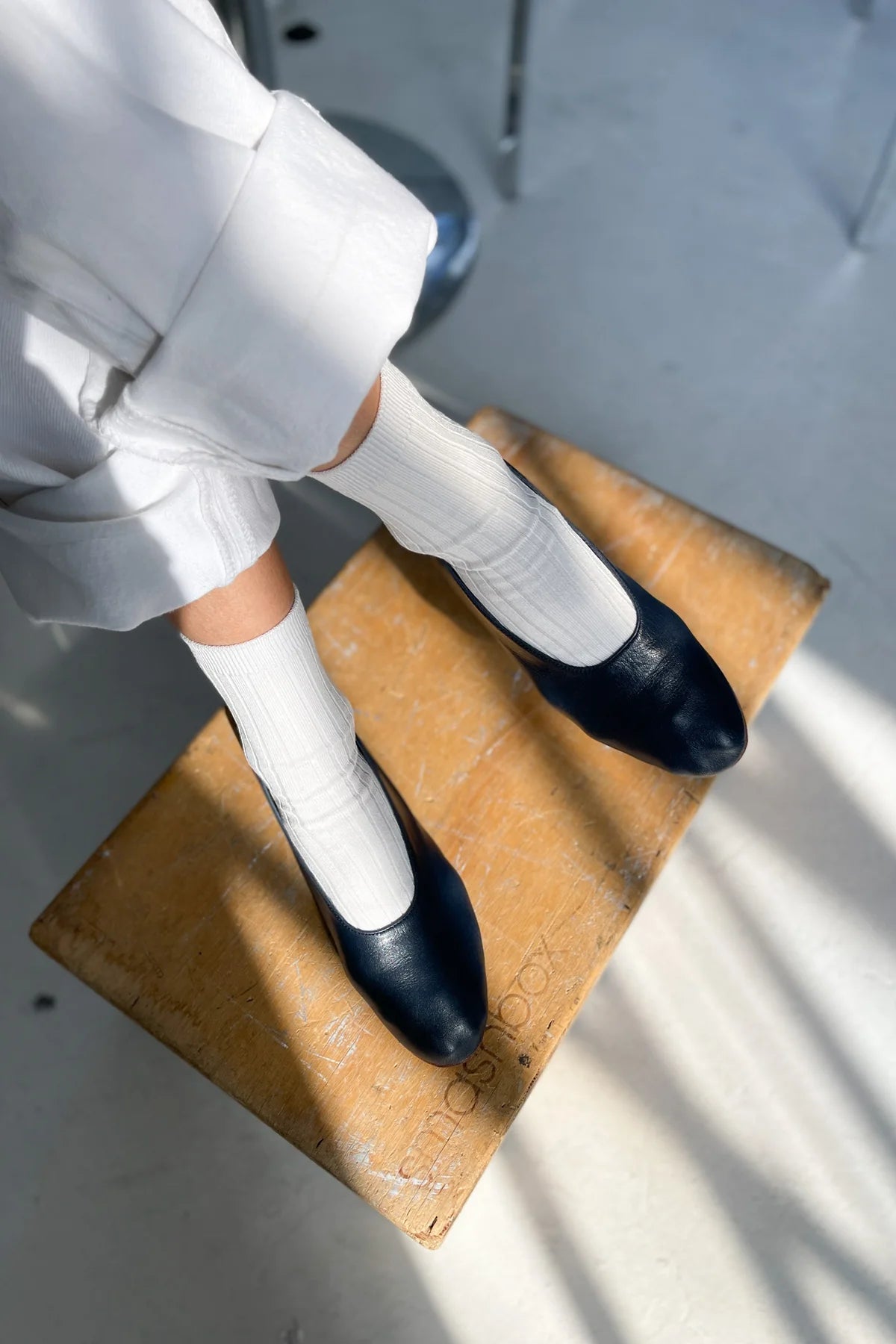 Person wearing black shoes and white socks on a wooden stool.