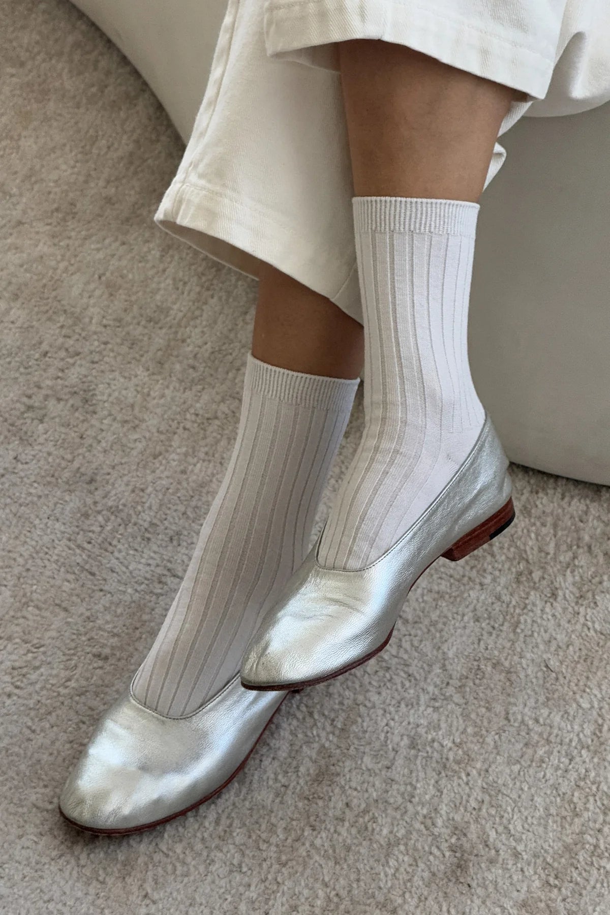 Silver metallic shoes worn with white socks on a neutral background