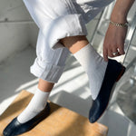 Person wearing navy loafers and white pants sitting on a wooden stool.