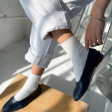 Person wearing navy loafers and white pants sitting on a wooden stool.