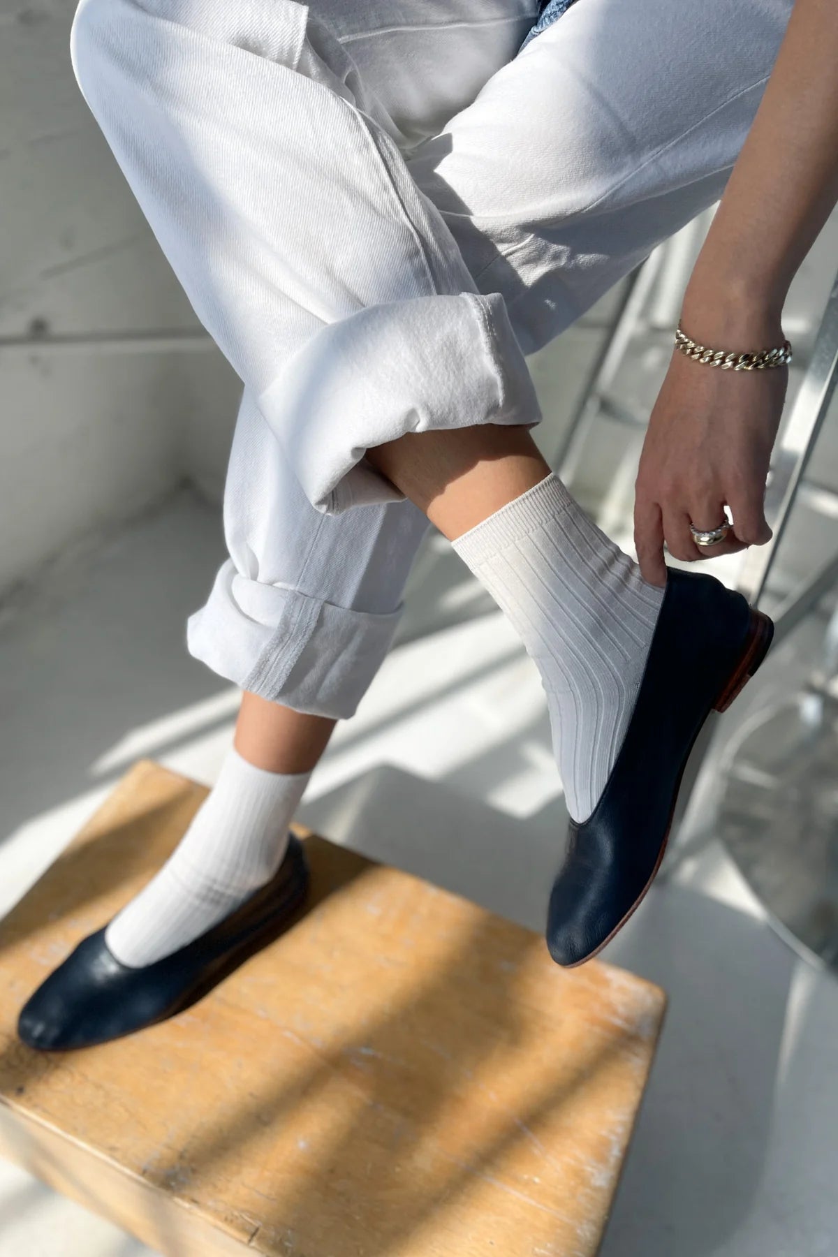 Person wearing navy loafers and white pants sitting on a wooden stool.
