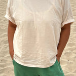 Person wearing a white t-shirt and green pants standing on sandy ground