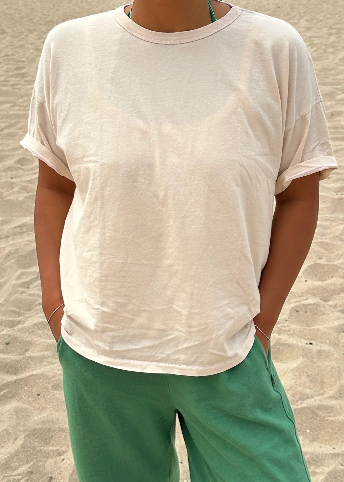 Person wearing a white t-shirt and green pants standing on sandy ground