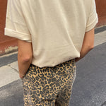 Person wearing a beige t-shirt and leopard print pants on a street.