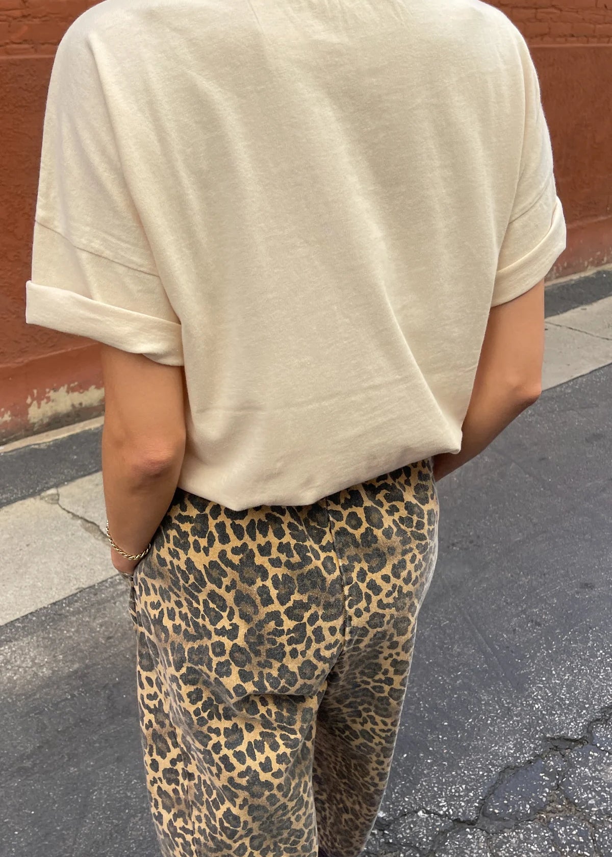 Person wearing a beige t-shirt and leopard print pants on a street.
