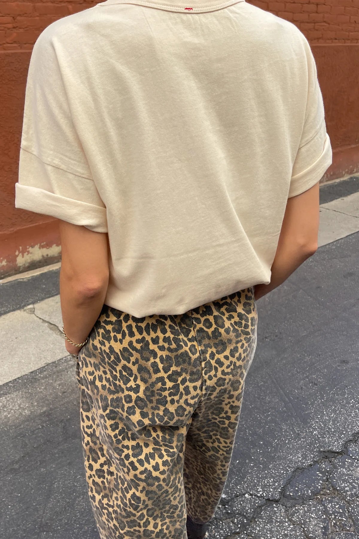 Person wearing a beige t-shirt and leopard print pants on a street.