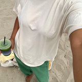 Person wearing a white t-shirt and green pants, holding a drink on a sandy surface.