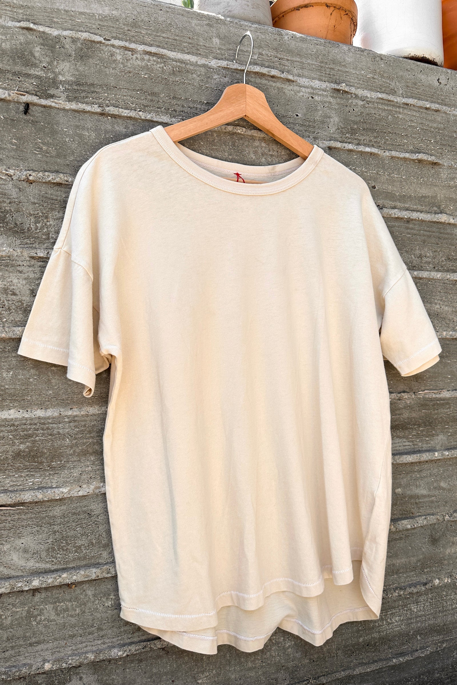 Beige t-shirt on a wooden hanger against a wooden background